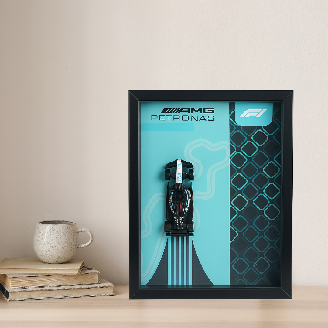Framed poster with AMG Petronas logo on a teal background, displayed on a wooden surface.